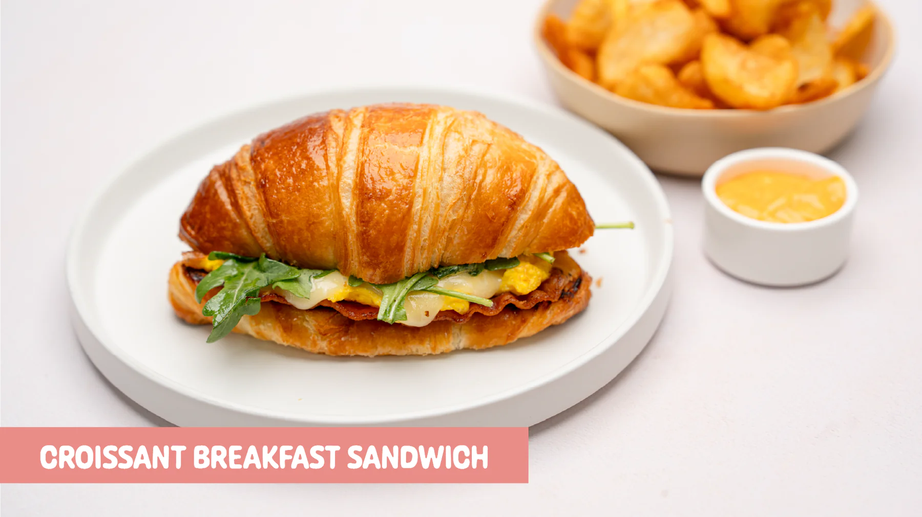 Buttery croissant breakfast sandwich with applewood bacon, scrambled egg, cheddar-jack-mozzarella, arugula, vinaigrette, and spicy mayo at Gud2Go Cafe, The Union in Garey, Pomona, CA.