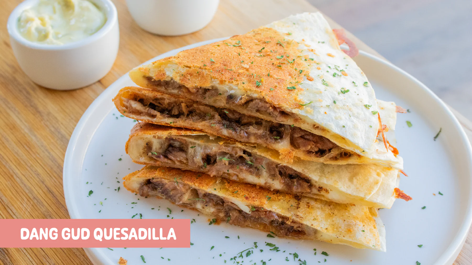 Crispy flour-tortilla quesadilla filled with Indonesian beef rendang, mozzarella, green chili mayo, tomato salsa, and crema fresca at Gud2Go Cafe, The Union in Garey, Pomona, CA.